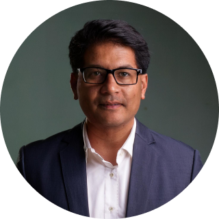 Portrait of Aarav Patel, a satisfied customer wearing glasses and business attire, confidently smiling.