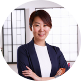 Portrait of Mei Lin Wong, a satisfied customer in business attire, smiling confidently with arms crossed.